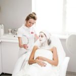 Beautician applying a facial mask to a client in a modern salon. Professional skincare service indoors.