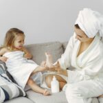 A mother and daughter enjoy bonding time on the sofa in cozy bathrobes, creating a warm family moment.