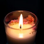 A beautifully lit artisan candle adorned with cherry blossoms, providing a warm and cozy ambiance.