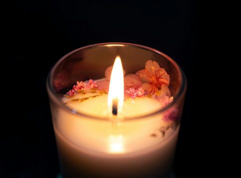 A beautifully lit artisan candle adorned with cherry blossoms, providing a warm and cozy ambiance.