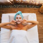 Woman enjoying a soothing spa treatment with a facial mask and towel indoors.