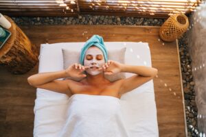 Woman enjoying a soothing spa treatment with a facial mask and towel indoors.