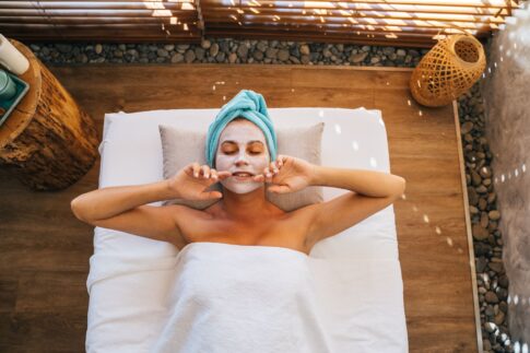 Woman enjoying a soothing spa treatment with a facial mask and towel indoors.