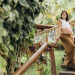 Pregnant woman enjoying a serene moment on wooden stairs surrounded by lush plants.