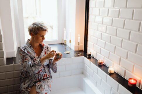 Woman in bathrobe enjoying aromatic candles for a serene bath experience.